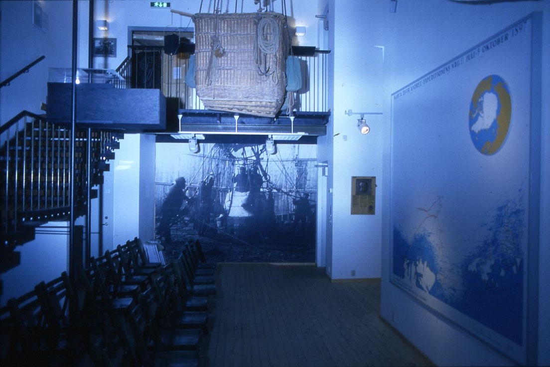 Interiör från Andréeutställning. Sveas ballongkorg i taket. En fondvägg med fotografi från startögonblicket.