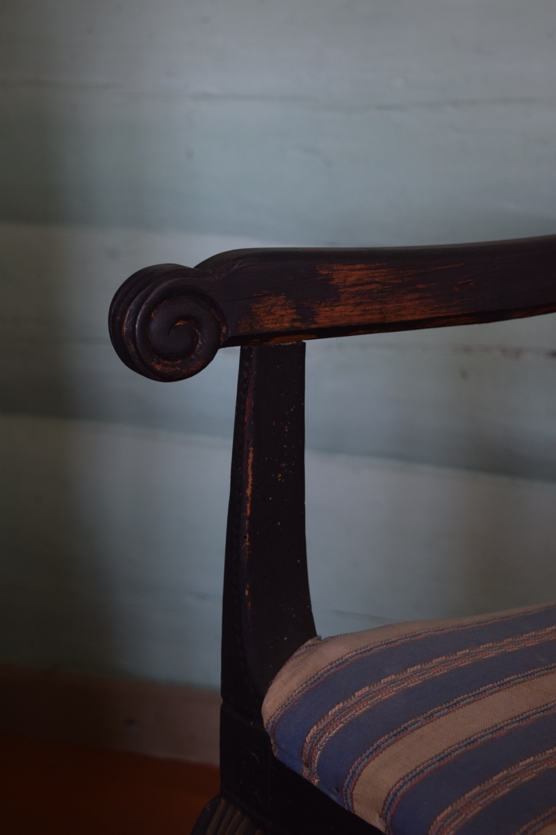 Sortmalt stol i tilnærmet rokokkostil (1700-årene) - bonderokoko. Midtfeltet i ryggen har blomsterdekor og initialer. Trekket er hjemmevevd i en blåfarge.