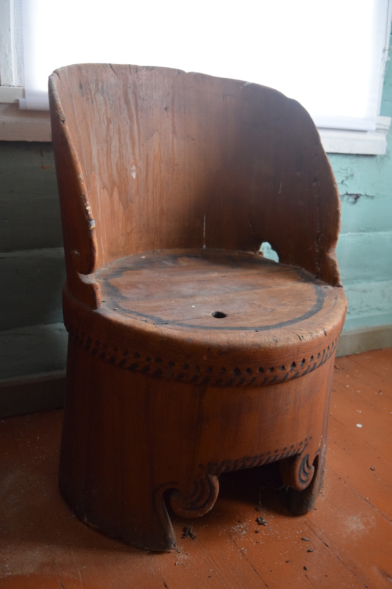 Hul kubbestol i furu. Stolen er lys brun med sorte ornamenter langs kantene