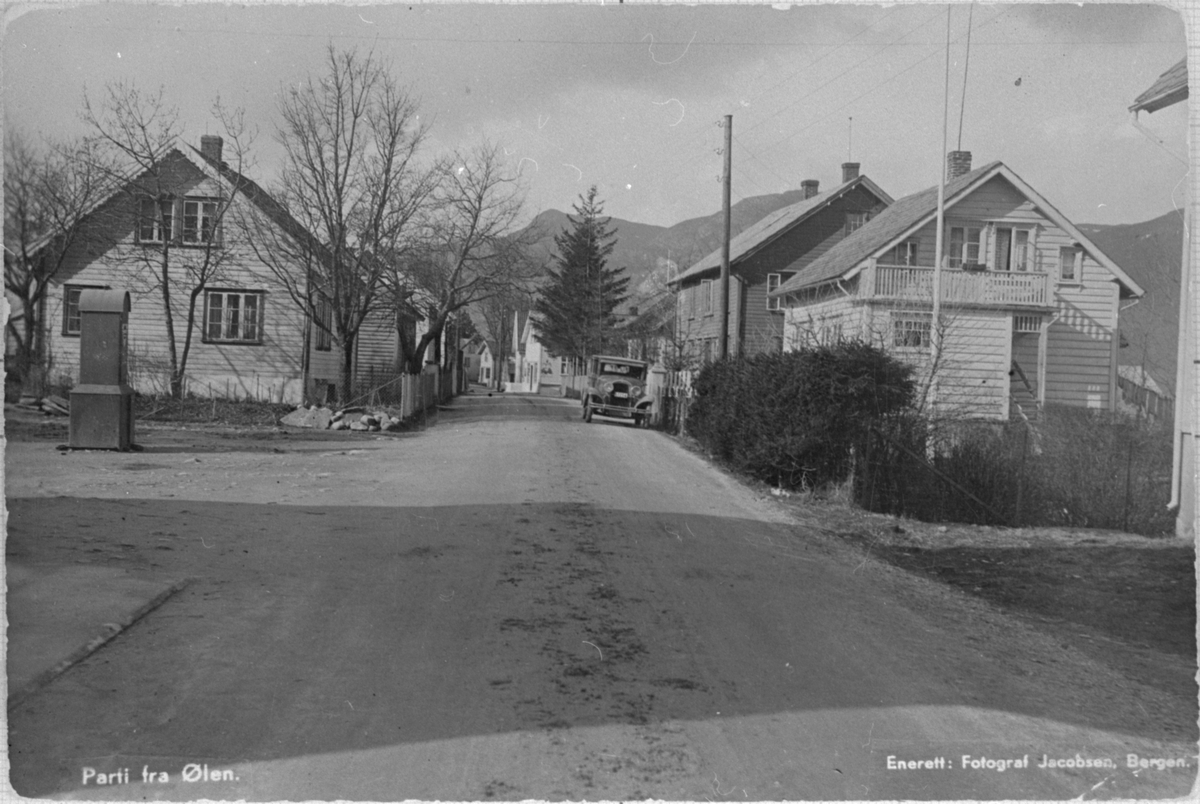 Postkort med motiv frå Sjoargarden i Ølen sett mot vest, ca. 1936. Til venstre er Helgesenhuset (Sjoargata 69). Til høgre er Urdal og Lundehuset (Sjoargata 66 og 68). Fleire av husa på biletet er framleis i bruk.