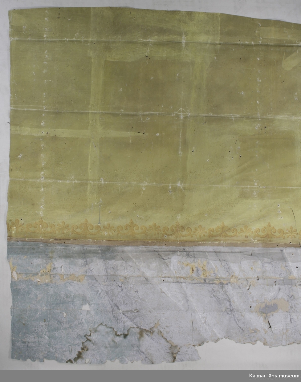 KLM 39925:6:1. Tapet av papper. Ett större väggfält och elva mindre bitar. Målad tapet med grön botten på två tredjedelar och schablontryckt bård i brunt och gult innan övergång till del med målad marmorimitation i grått och grönblått, eventuellt samtida. På de mindre bitarna finns fragment av flera ovanliggande tapetlager med andra mönster, bland annat en bård, bredd cirka 11 cm, med grå drapering och gulbruna rosor och kransar med schweinfurtergröna blad. Närmast ovanpå denna sitter fragment av tryckt tapet med bruna och röda blommor på satinerad beige botten. Ovanpå denna sitter fragment av velourbård i svart och brunt. Över denna en tryckt tapet med svart botten och nästan yttäckande blom- och bladmönster i bruna färger och guld, KLM 39925:6:2. Överst av tapetlagren sitter en tryckt tapet med ljusgrön botten och vissa utsparade ytor. Gulddetaljer i lodräta fältindelningar.