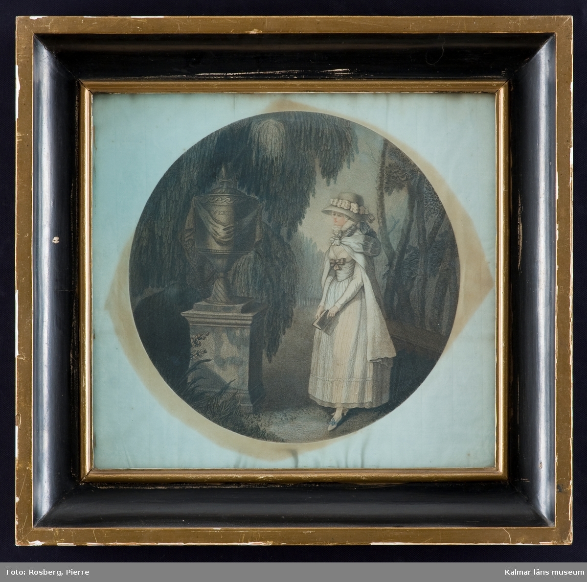 Motivet föreställer en ung dam klädd i 1700-talskläder. Hon bär en bok i handen och står framför ett podium med en urna.