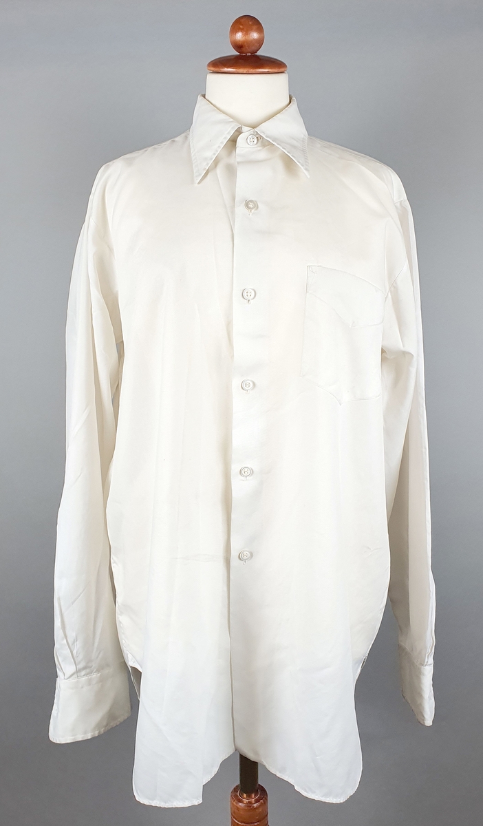 Hvit skjorte med lomme på venstre bryst. Spisse skjortekrager og mansjetter med knapper.