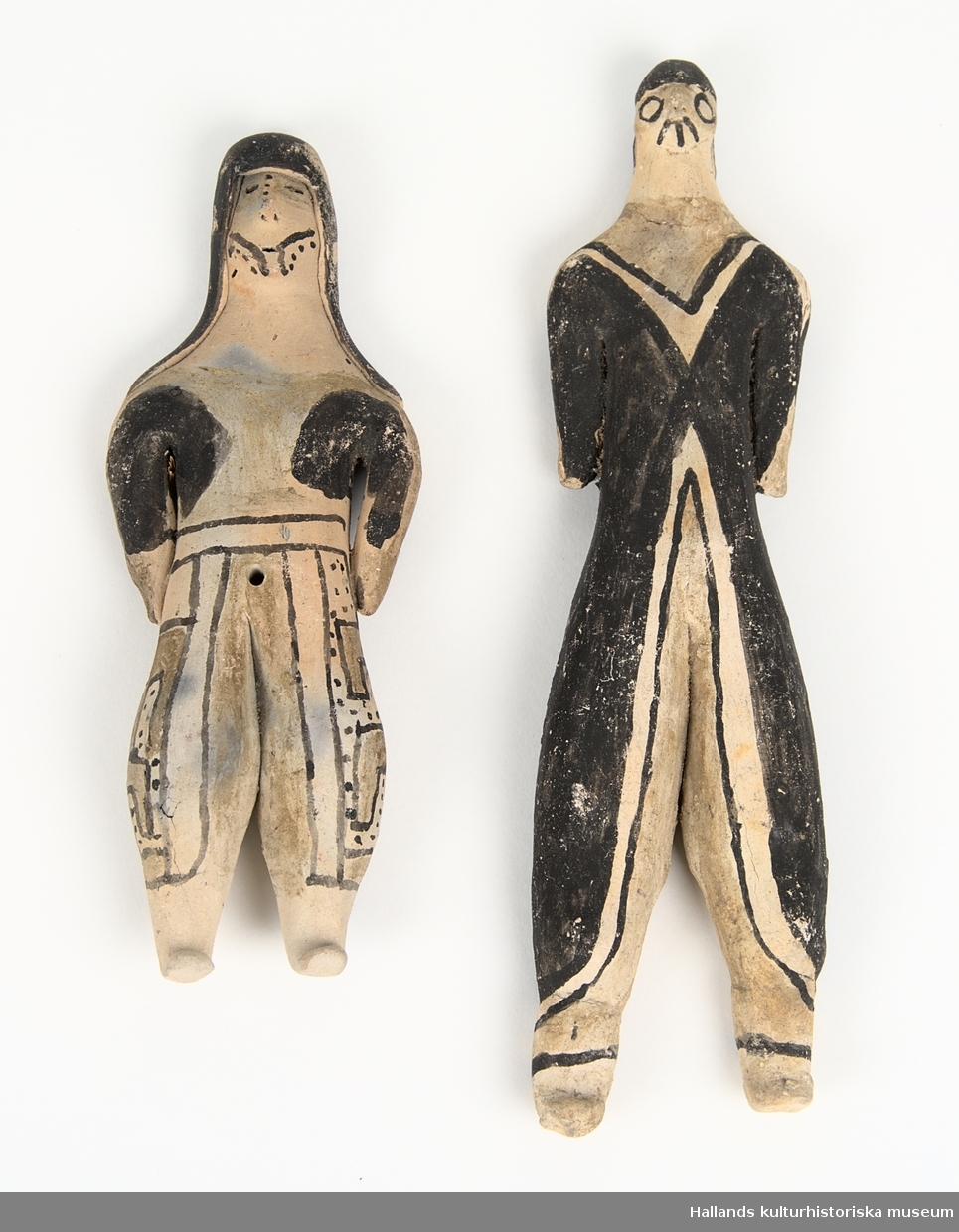 Två människofiguriner av ljus keramik. Delvis bemålade med svart färgpigment.