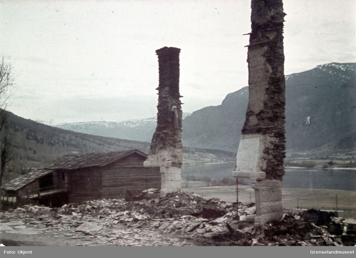 To piperester står i en ruin. I bakgrunnen står en hel bygning med skifertak. 