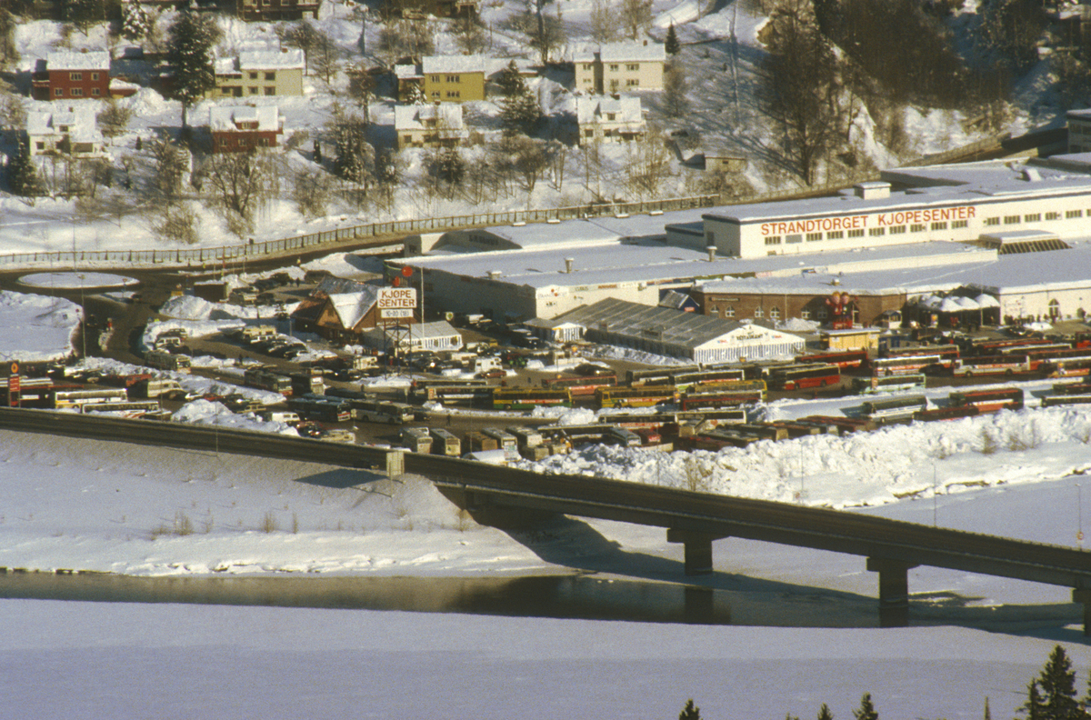 Lillehammer. Strandtorget, som ble brukt som bussterminal under OL 1994. Lillehammer bru og Gudbrandsdalslågen i forgrunnen. Nedre del av Busmoen i bakgrunnen. Utsikt mot øst fra Saksumsdalsvegen.