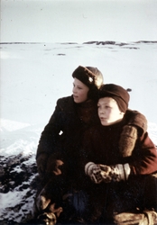 To unge gutter sitter på en knaus i et snødekt landskap.