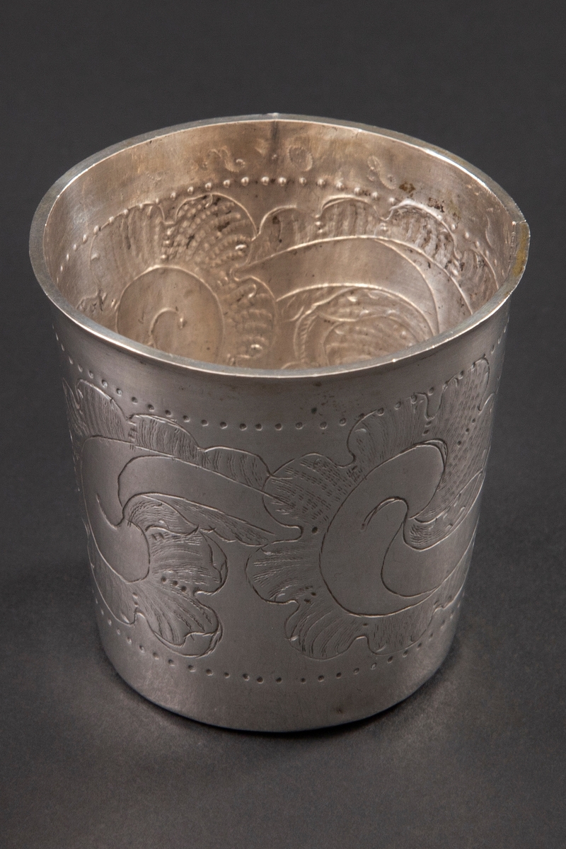 Beger i sølv med svakt konisk form. Korpus er dekorert med punslet og gravert stilisert rankedekor.