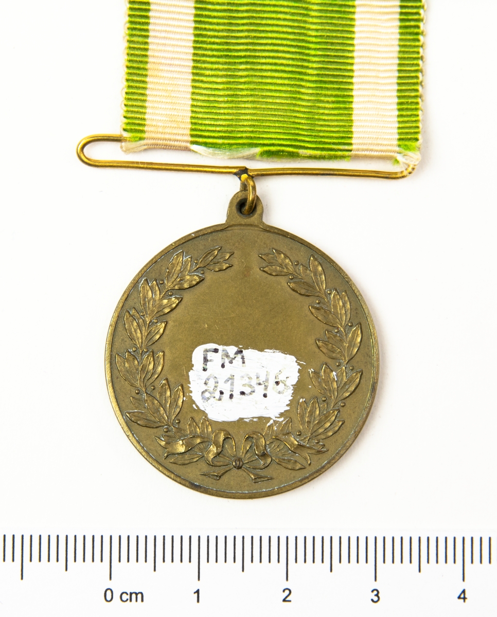 Medalj med band i vitt och grönt. På medaljens ena sida finns en lagerkrans med I F S i mitten. På frånsidan finns en lagerkrans.