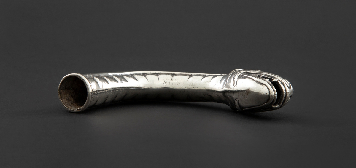 Skafthåndtak til paraply i sølv. Den er støpt, hul og formet som et dragehode med kraftig svungen hals. Halsen danner selve håndgrepet.