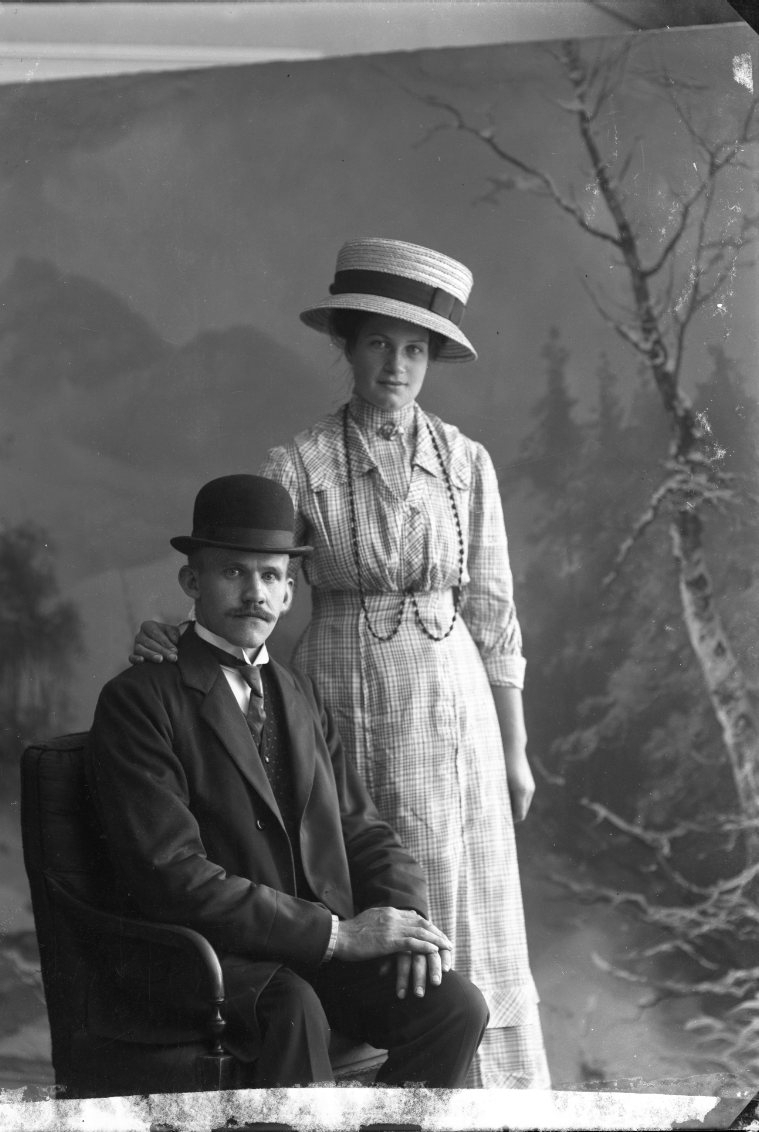 En ung kvinnna och man, bägge med hatt. Mannen sitter på en stol, hon står bredvid med höger hand på hans vänstra axel. Mannen är Axel Ström från Reaby, Gränna socken. Kvinnan är sannolikt hans hustru Ida Charlotta Bom.