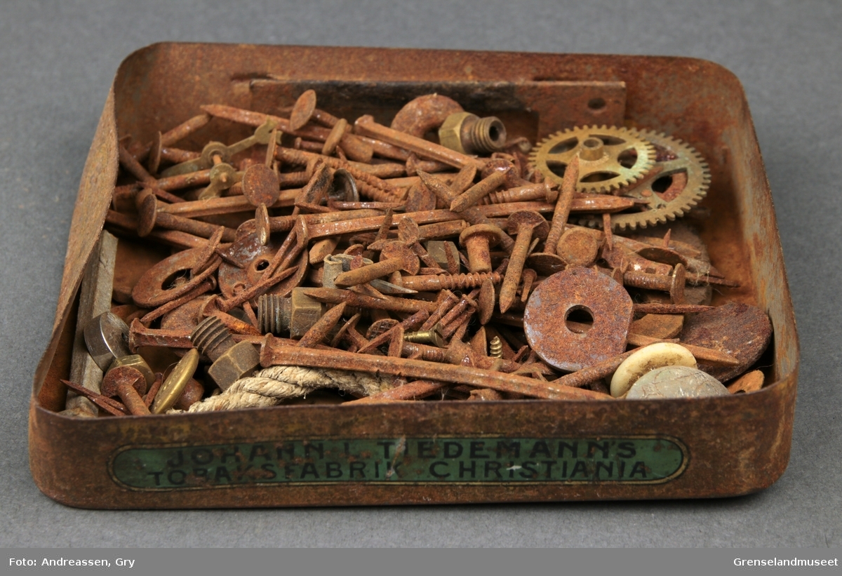 Tobakkseske i metall fyllt med sm[ spiker, stifter, tannhjul, muttere, knapper og skruer. Alt rustet.