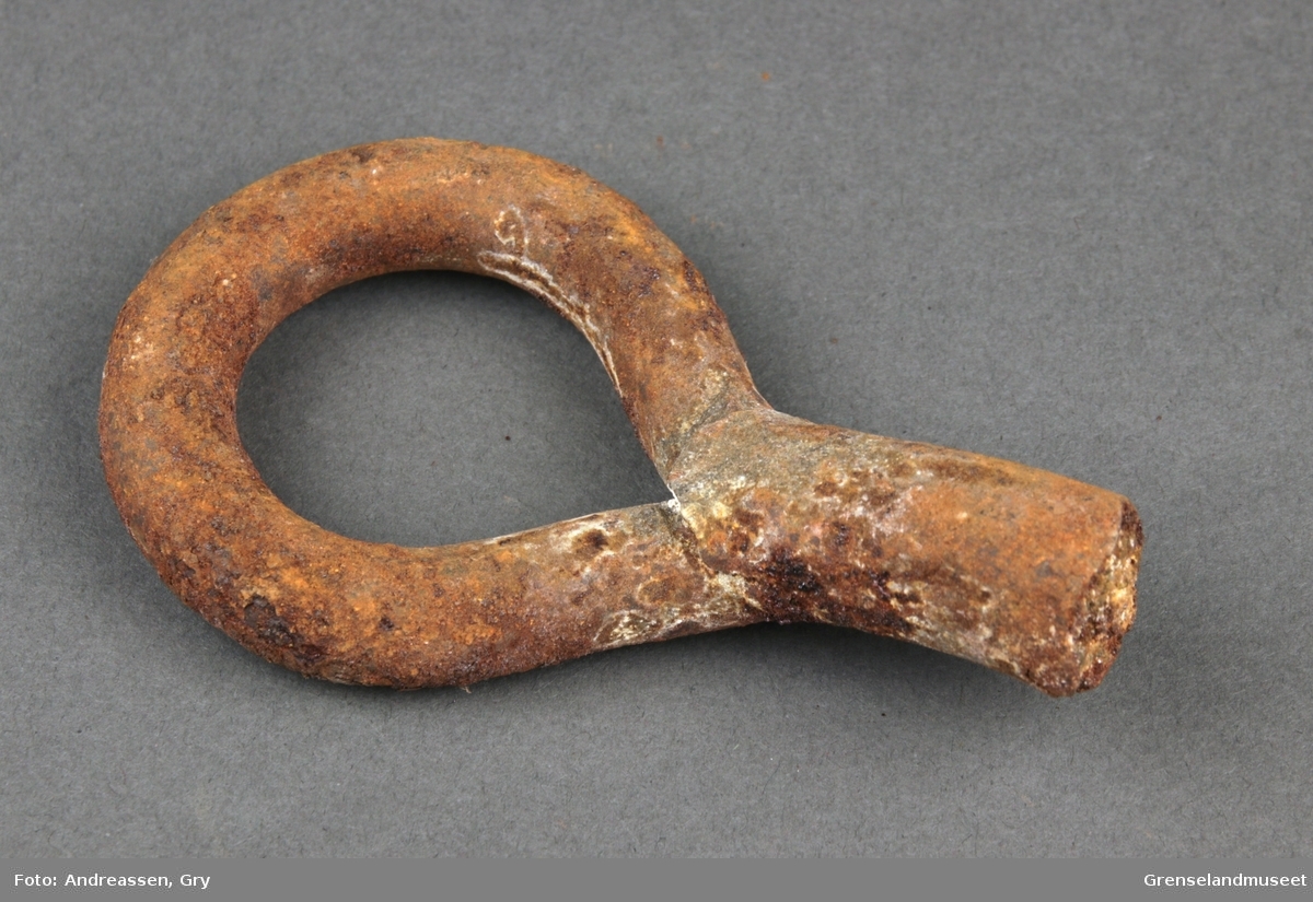 En øyebolt i jern, ringen er inntakt men selve bolten eller kroken er knukket av. Rusten.