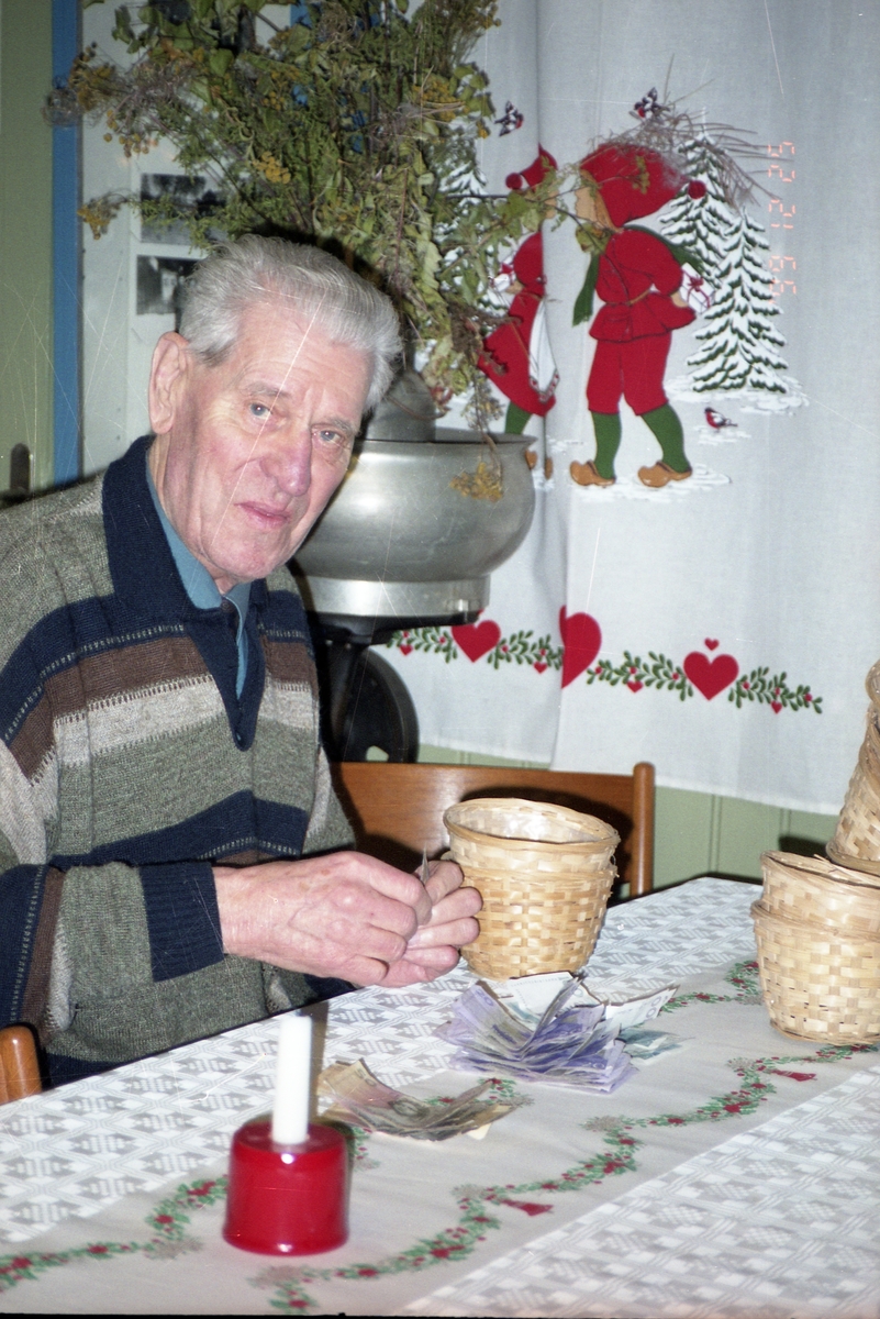 En man sitter vid ett bord med julduk och ljusstake och räknar pengar. Öppningen av Bollnäs-kistan, juldagen 1999.