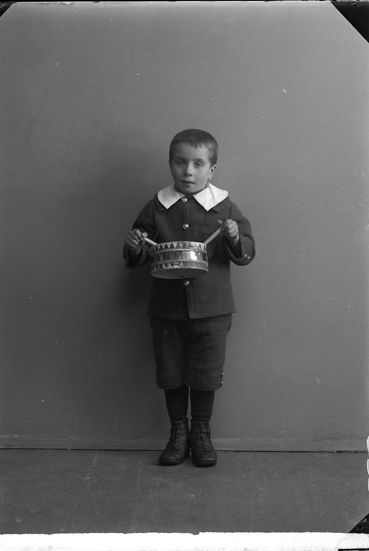 Porträtt av en liten pojke med en trumma runt halsen.