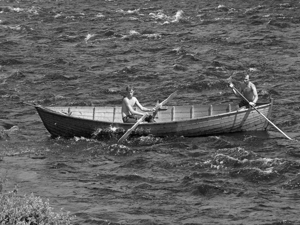 Sluttrensk i elva Stor-Grøna i Trysil, Hedmark. Fløtere i båt underveis for å løsne tømmer som har lagt seg langs elvebredden.