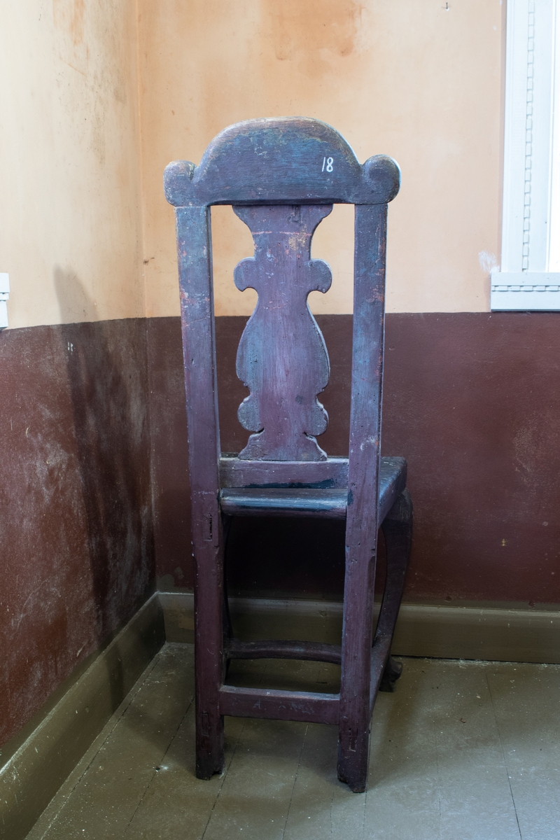 Hjemmelaget stol med rokokko stil og utskjæringer med renessanse preg på ryggen hvor det er rike utskjæringer med et hode. Rødbrun maling.