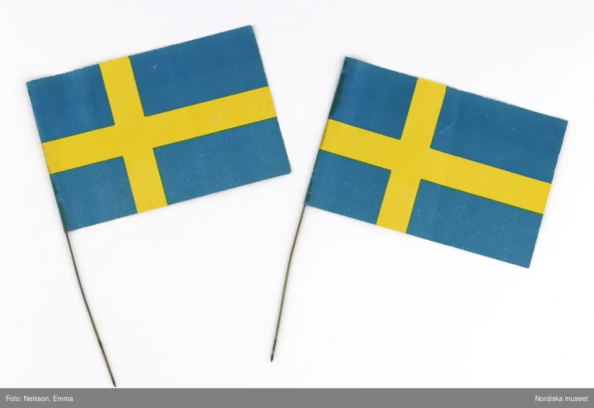 Fyra stycken (a-d) julgransflaggor föreställande den blå-gula svenska flaggan. Två stycken var placerade på var sida om julgranens topp. Av papper med metallstång som fastsättningsanordning.

Lena Kättström Höök 2019-03-21