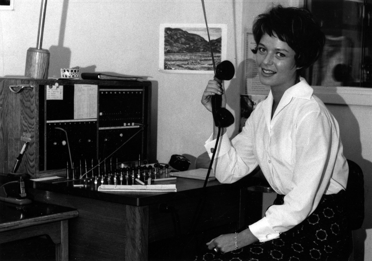 Margaretha Bruto sitter, vänd mot kameran med telefonluren i högra hand, vid telefonväxeln i Kabeldons reception på Plangatan.