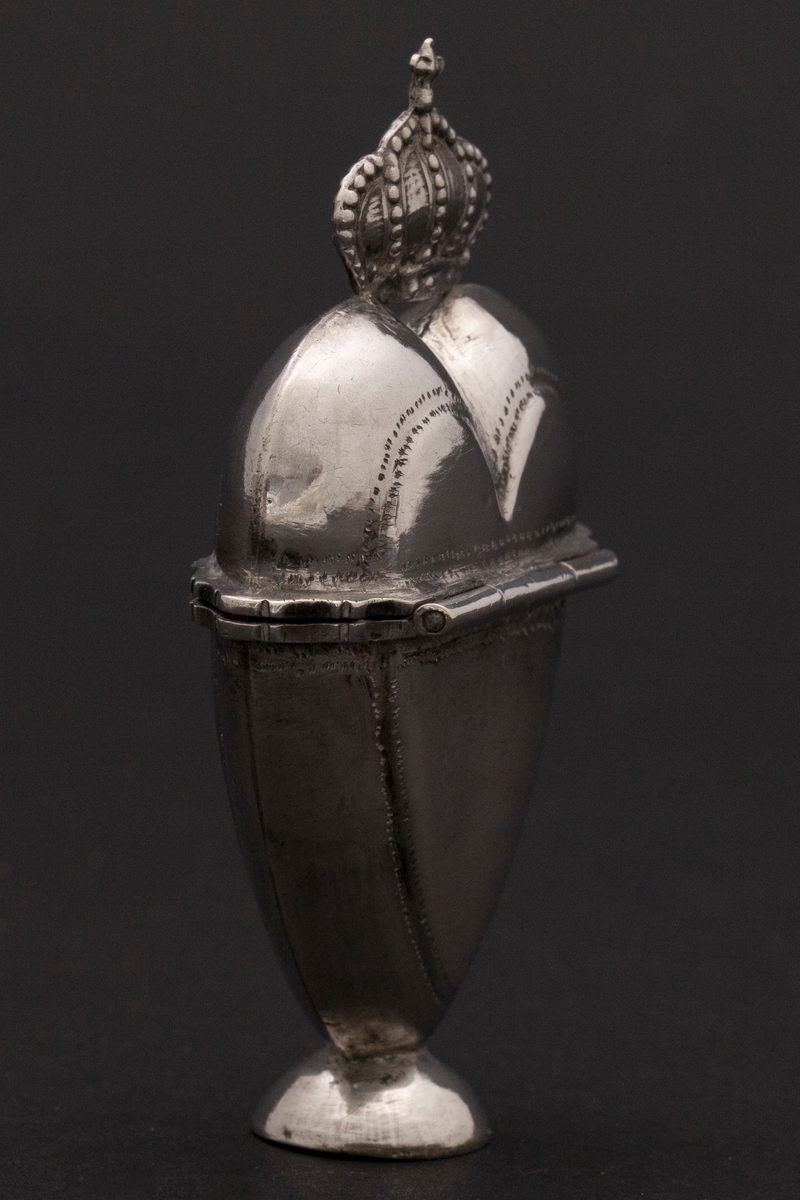 Hjerteformet luktevannshus i sølv med liten, rund fot og krone med kors på lokket. Profilert kant langs munning og lokk. Enkel prikkdekor. Innvendig forgylt. Svamp på innsiden.