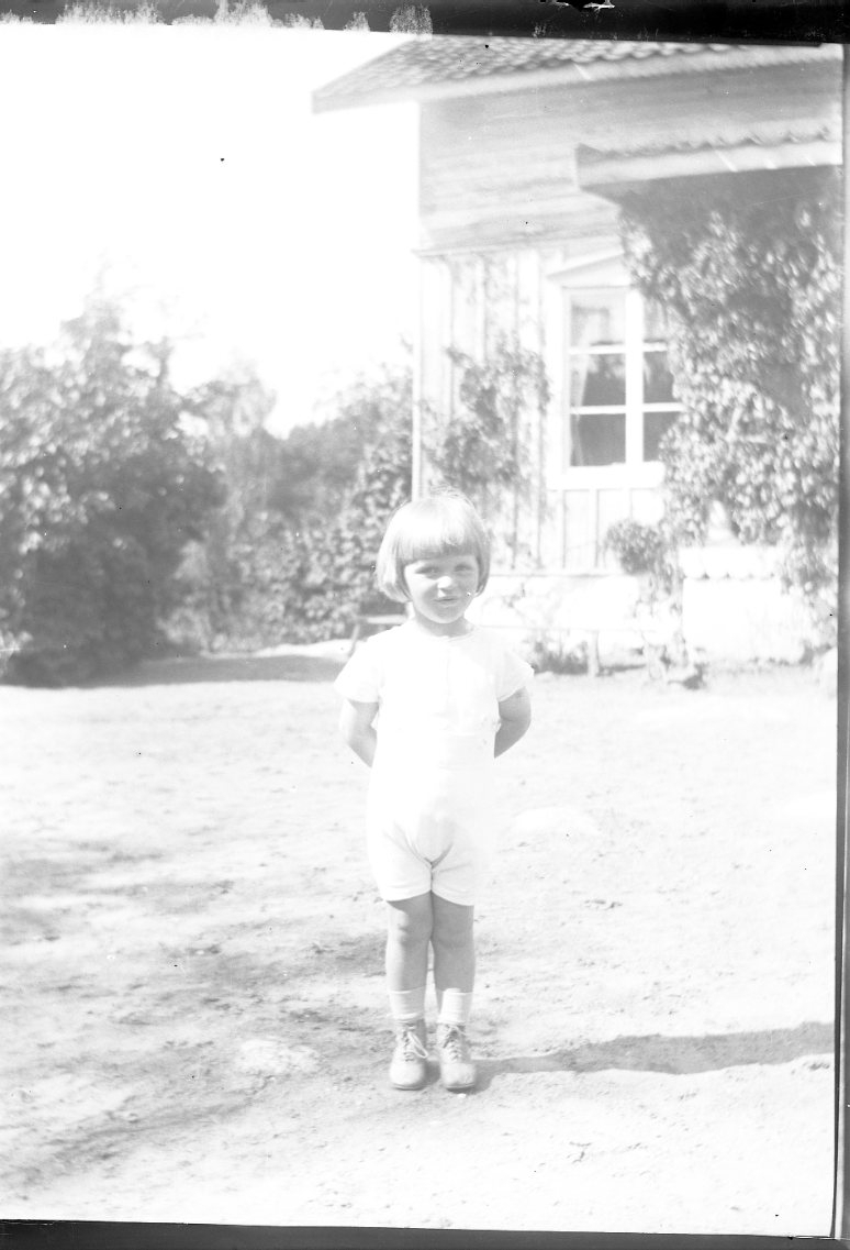 Ett barn står på en gårdsplan vänd mot fotografen. Det är sommar. Troligen "gossen Falkenberg".