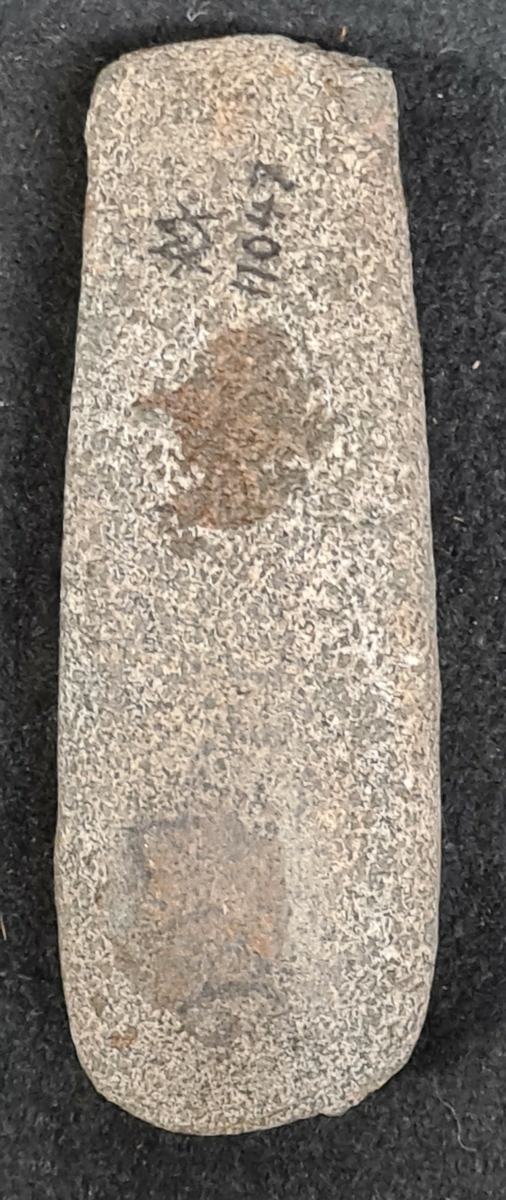 11 047 Forshälla socken, Bohuslän.

Yxa bergart, 1 st, fläckig. Rak nacke, spetsig slipad egg. Kilformad. Vittrad. L. 12,3 cm, br. 3,5 cm