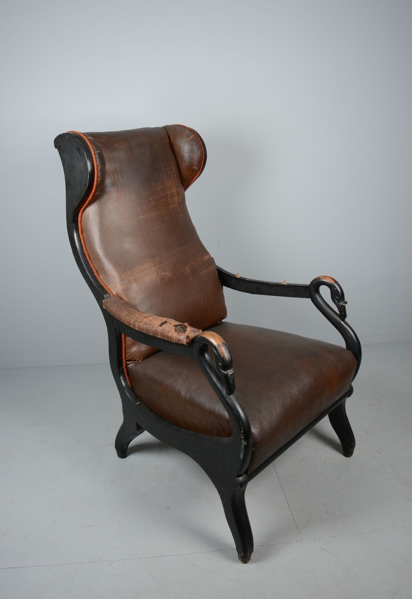 Ørelappstol med åpne, polstrede armlener, med støtter formet som svanehoder. Agramanbånd langs sidene på ryggen. Fjæring i sete.