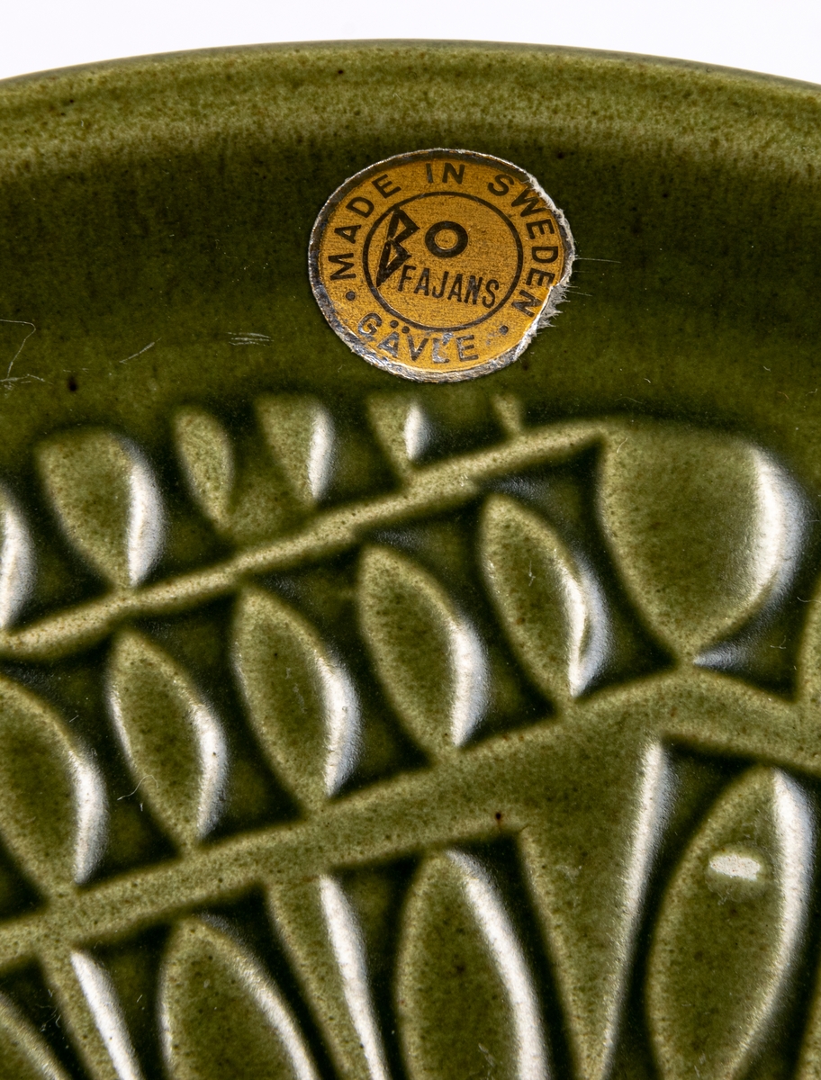 Assiett i lergods, olivgrön glasyr med bladliknande djuptryckt mönster.
