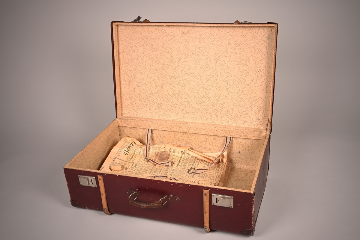 Koffert i rødbrunt skinn med låser av metall. To trebeslag er festet rundt koffertens kropp, og hjørnene er sikret med metallbeslag.