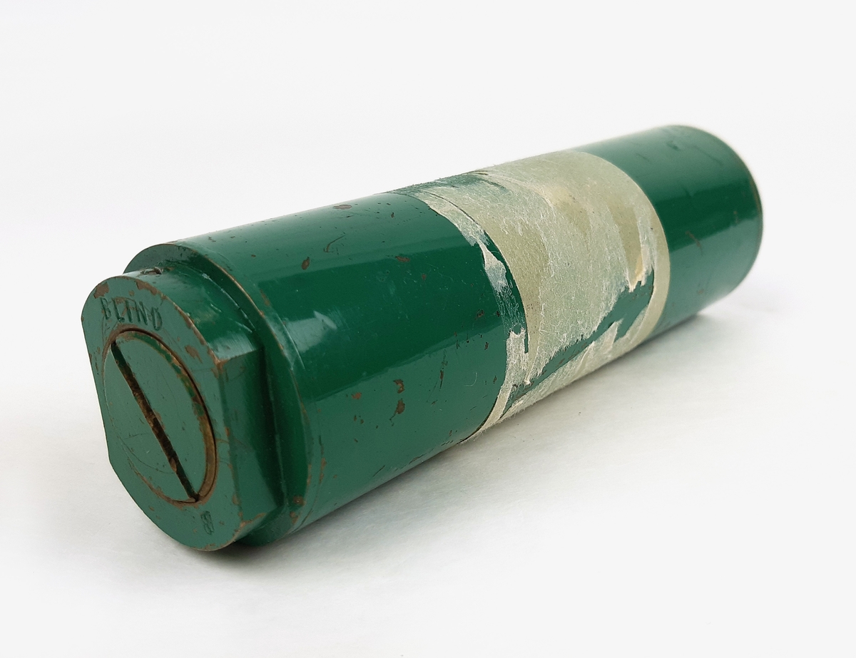 Tändpatron m/51, bestående av en cylinderformad kapsell i grönmålad metall. Vid sidan märkt "Tändpatron m/51". Samt märkt "BLIND" på kortsidorna.