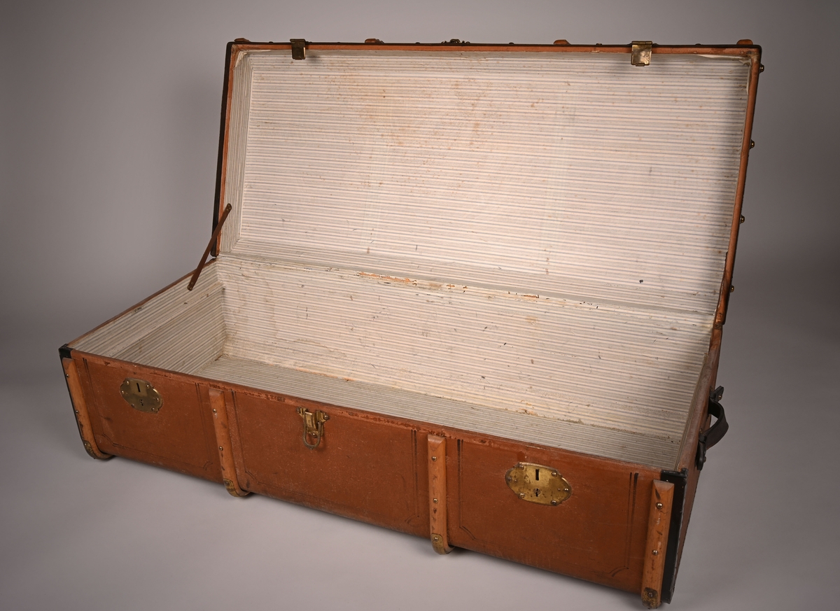 Koffert laget av tre, papp og skinn. Innsiden er kledd med papir. Den lukkes i front med tre beslag. På sidene er det festet bærehåndtak av skinn.
