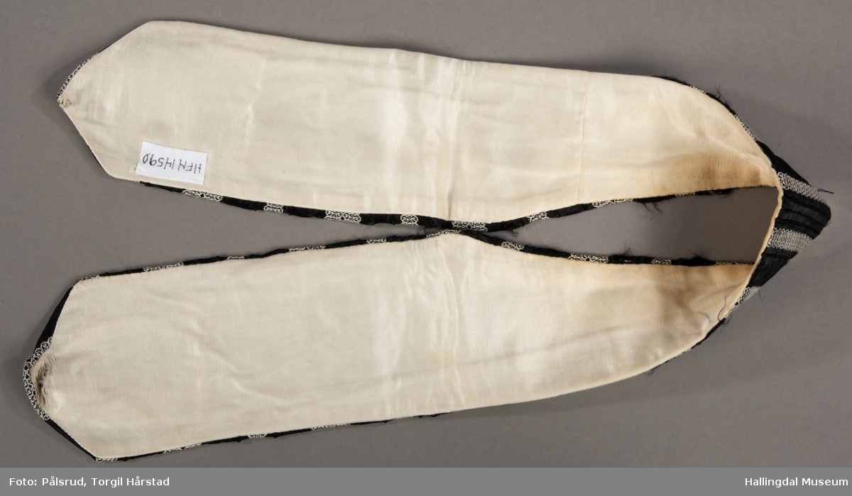 En løsthengende krage i silke/bomull med stripet mønster i hvitt på sort bunn - border. Hvit fôr. Slitte ender.
