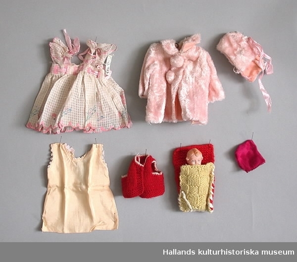 Dockväska av trä, grönmålad. Innehåller två dockor, dockkläder samt tillbehör till dockorna. Uppfälld bildar väskan en dockgarderob.