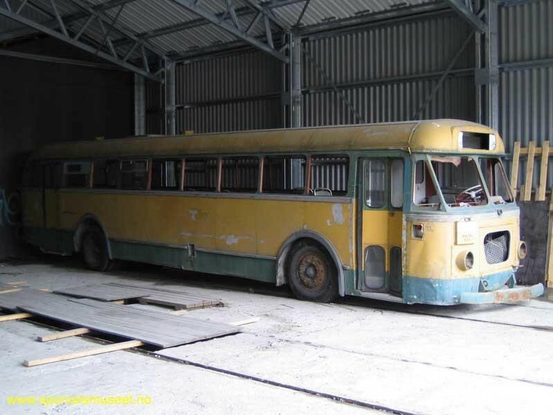 Gul buss med grønne bånd på nedre del og rundt vinduene. Det er inngangs- og utgangspartier i front og bak på langsiden. 