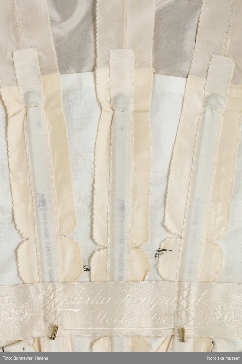 Tvådelad klänning monterad på docka. NK:s Franska damskrädderi.
Tvådelad, korsetterad klänning av vit taft överdragen av svart tyll och spetsar. Klänningen bars av Lydia Maria Bring född Widman (1855-1939) vid en fest på Gripsholm 1904.