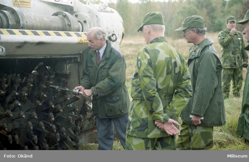 Försöksvagn (stridsvagn 103) med ”minröjningsaggregat Gluff-Gluff”.

På bilden är försöksledare från FMV, C FarbC överste Björn Svensson, Hans Majestät Konungen Carl XVI Gustaf, löjtnant Leif Wisén, och general Curt Sjöö.