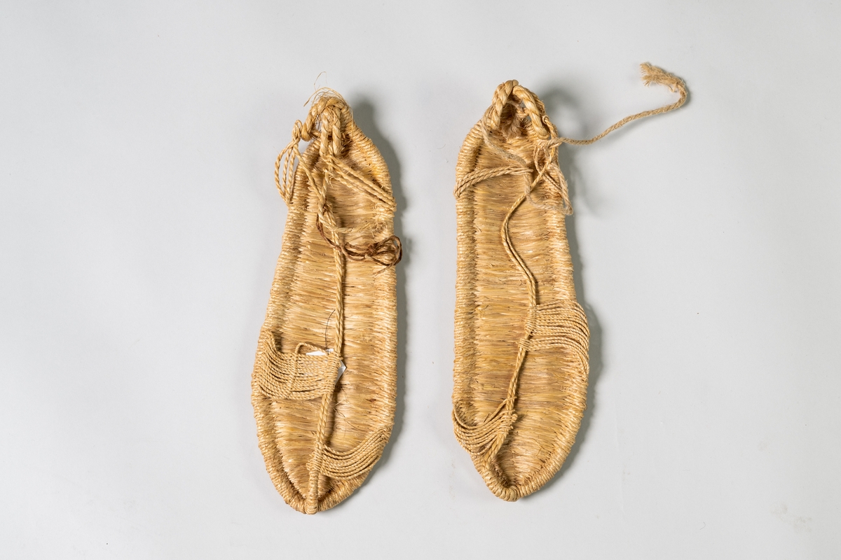Skor, till mansdräkt från Kina, ett par sandaler av bambu. Sandalen består av en flätad sula och snörning från hälögglor fram till tårna.

Papperslapp, A5, med anteckningar från givaren är fäst på en sandal. Samhör med JM.55406:1-8.

Se Historik.