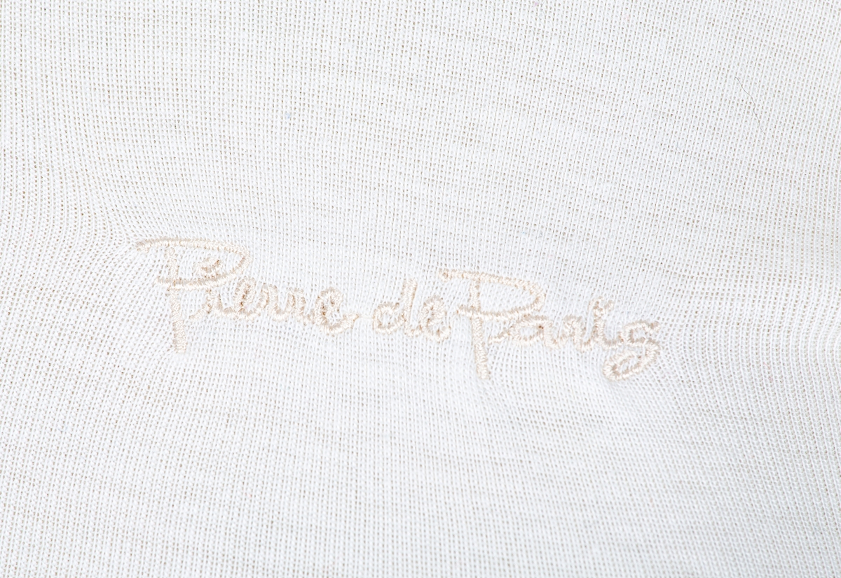 Pologenser. Kremhvit. Nedbrettet hals. Lange isydde ermer.  Signaturen Piere de Paris maskinsydd foran.
ca 1980. Pyntet bruk gjennom flere år. Brukt sammen med FHM.06824 og 06825.