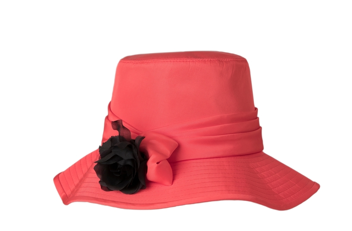 Rosa-röd damhatt av acetat, med hög, rak kulle, vågigt helstickat brätte, som är bandkantat av samma tyg. Monterad med en drapering med en svart blomma. Svart foder inuti. Foderband av rött ripsband. Isydda etiketter: "wigéns 56 MADE IN SWEDEN", och "wigéns, 23002". Inne i hatten finns även klisteretikett märkt: "78".