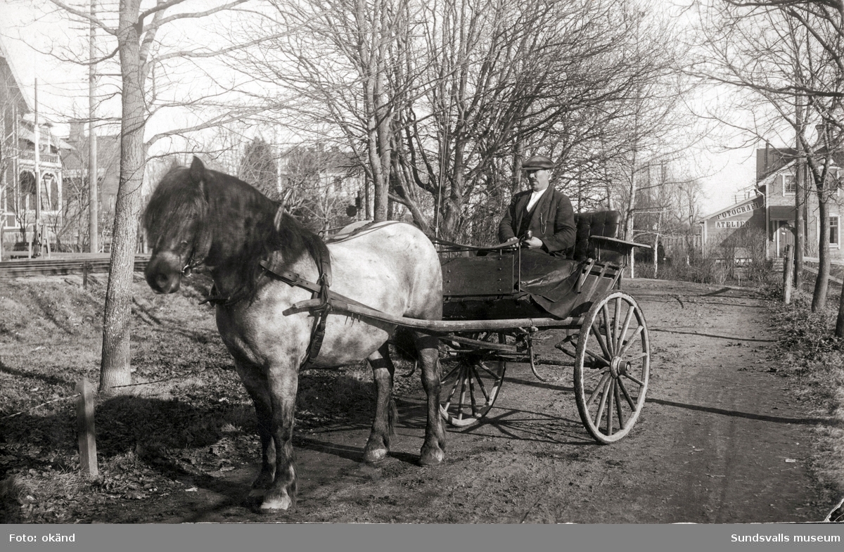 Vykort poststämplat 1923 till Fröken Beda Jönsson, Stöde (Mf Handl Höglunds Post). Avsändare J.K. Motivet är en man i en tvåhjulig vagn spänd bakom en häst, en järnväg syns till vänster, bostadshus vid sidorna varav ett med skylt: Fotografi Atelier.