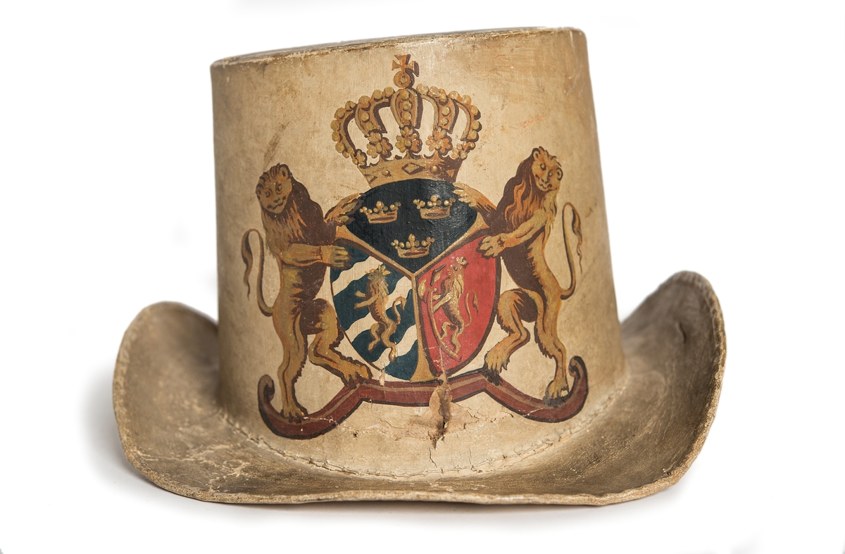 Hatt tillverkad av papp som målats med en crémegul färg. Framtill försedd med svensk-norska riksvapnet i färg. Foder av bomullstyg, 115 mm brett och dragsko.