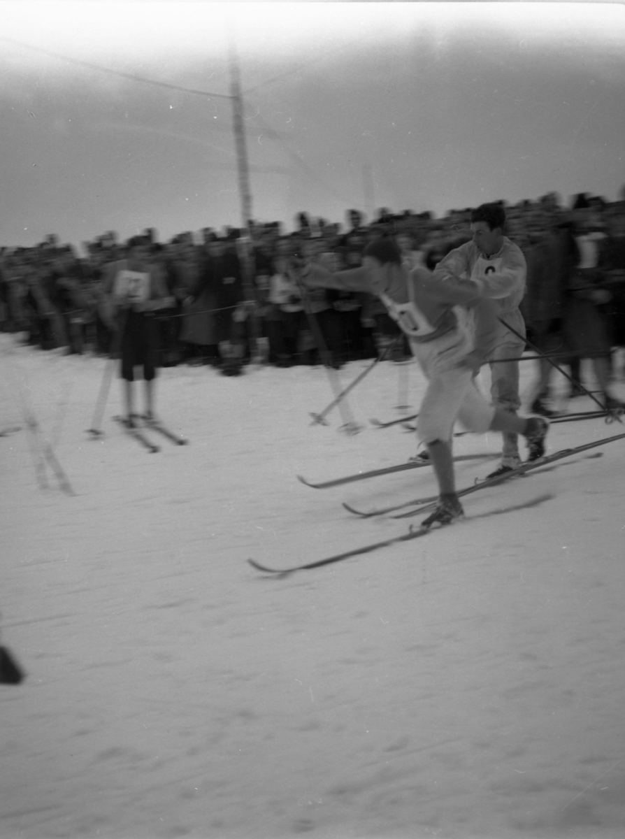To skiløpere slåss om plassen i løypa. Mange tilskuere sees i bakgrunnen.