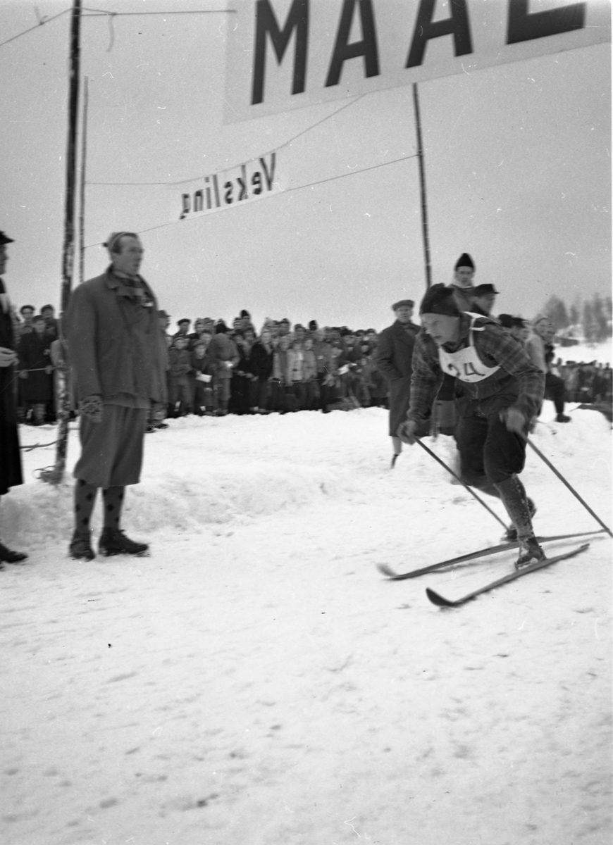 En skiløper med startnummer tjuefire i full fart i løypa. Mange tilskuere sees i bakgrunnen.