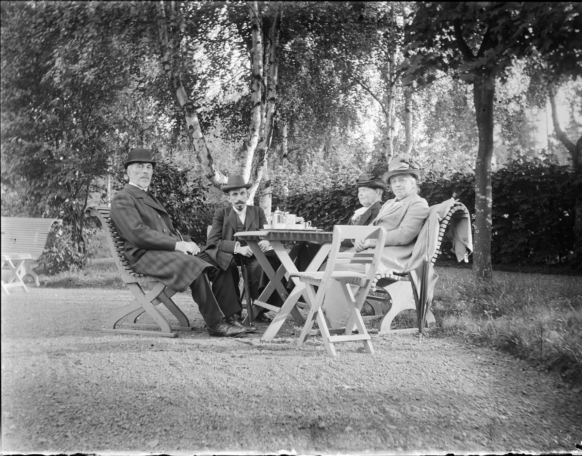 Fyra personer sitter vid kaffebord i trädgården