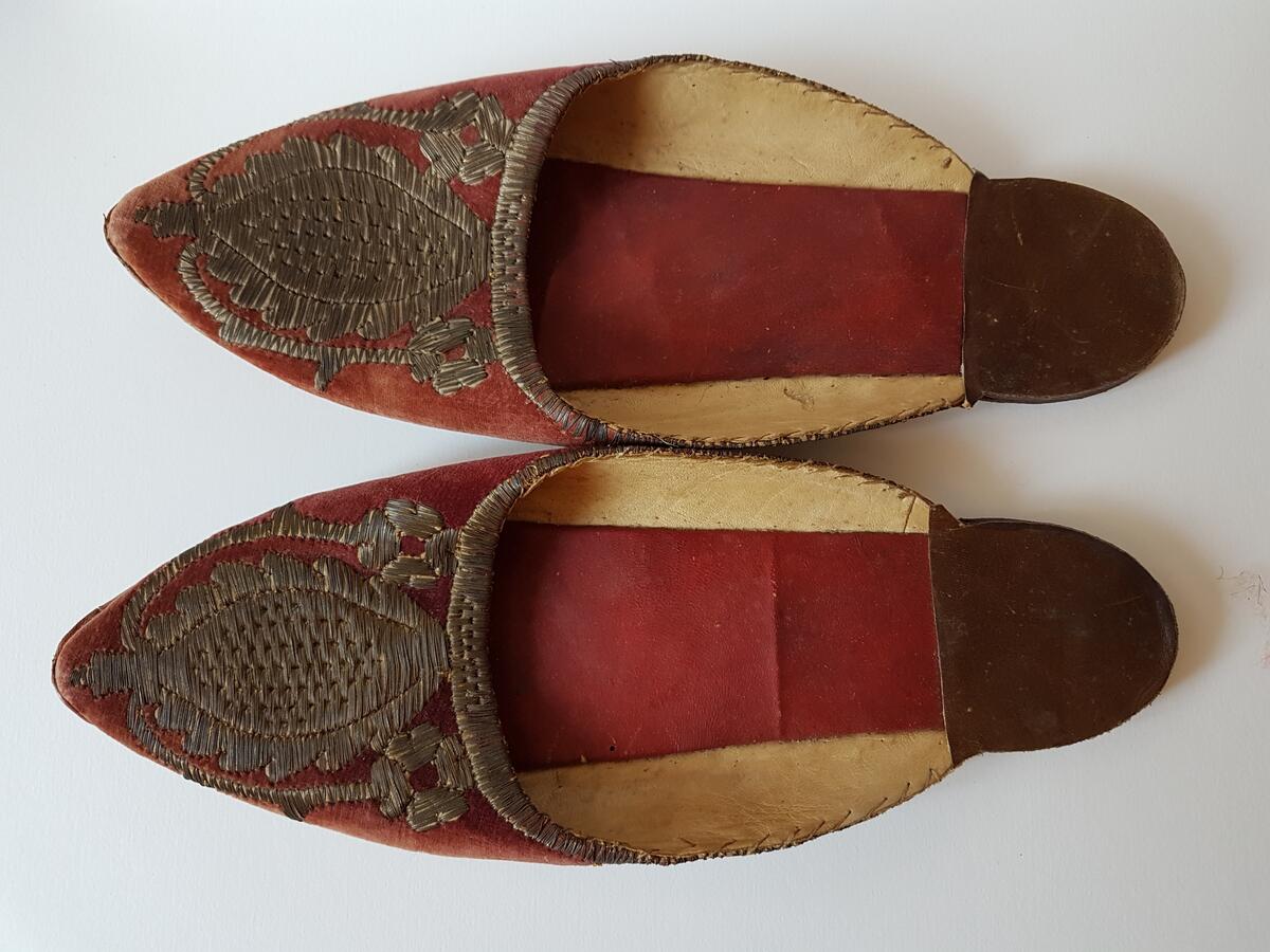 Ett par skor, tofflor i röd färg med broderad blomsterdekor. Tofflorna kommer troligen från Turkiet.