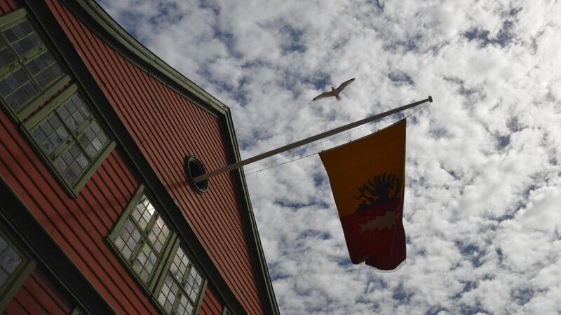 Bilde av det hanseatiske flagget som vaier i vinden, på stang ut fra et bryggehus.