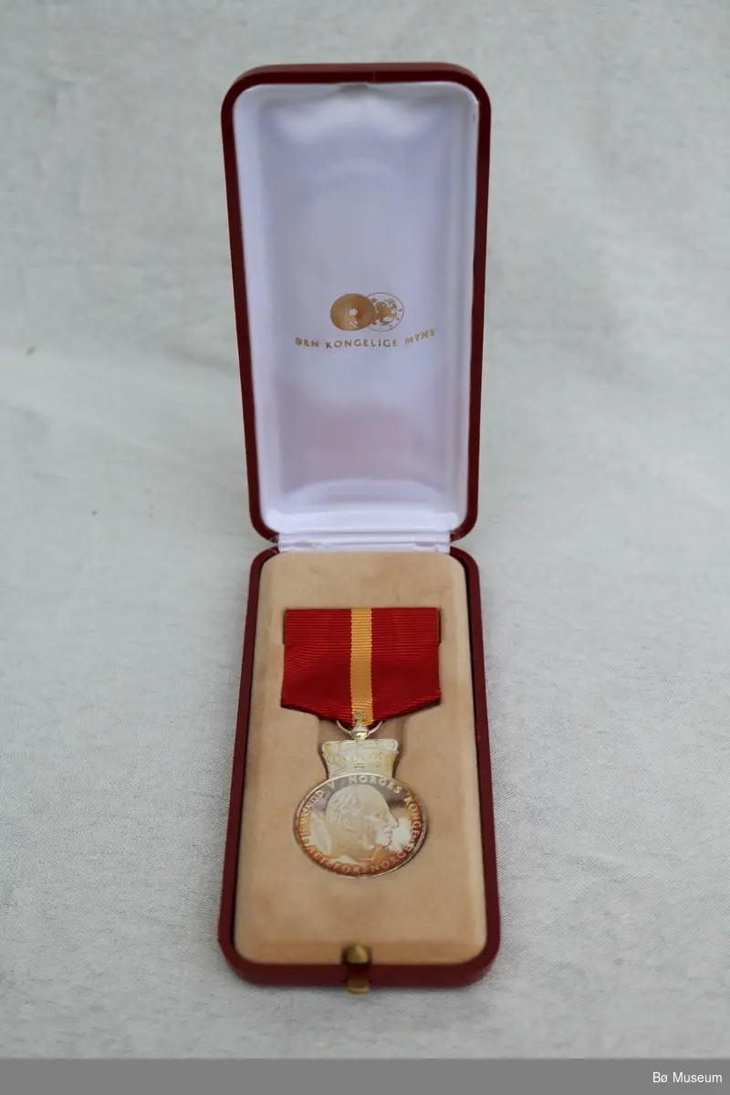 Konges fortjenestemedlaje i sølv (a), tildelt Randi Staurheim. Medalje ligg i originalt etui (b). Tilhøyrande diplom i ramme (c).