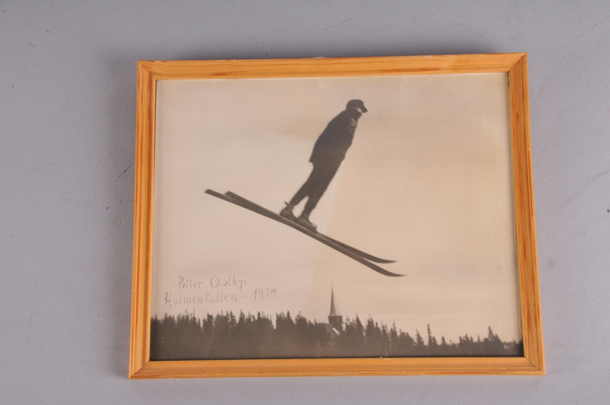 Bilete av peter Østbye som hoppar på ski i Holmekollen i 1914. Biletet ligg laust mellom glas og bakplate.