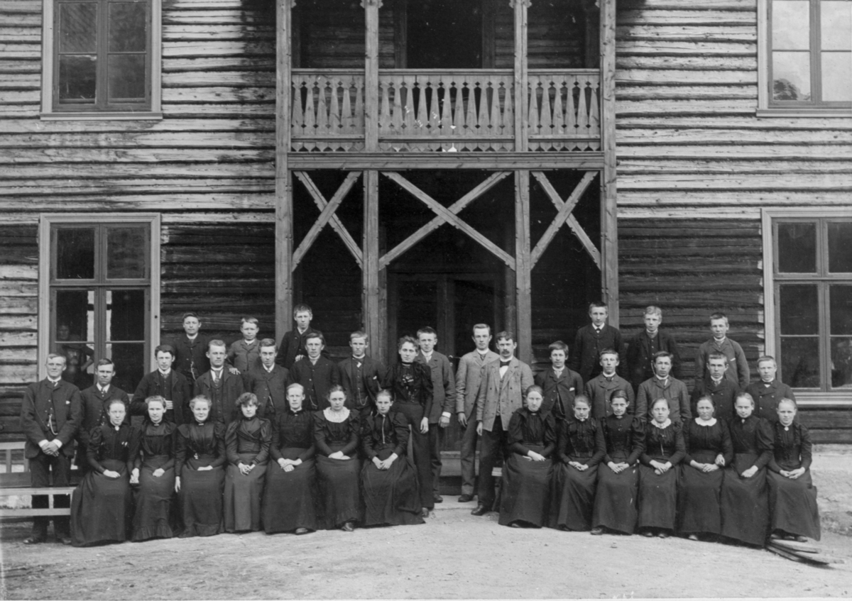 Klassebilde av den første Framhaldsskolen i Sigdal. Rektor Burkjebø med elever, foran borgerstua i Prestfoss. Antagelig slutten av 1890-tallet, siden borgerstua er ukledd.