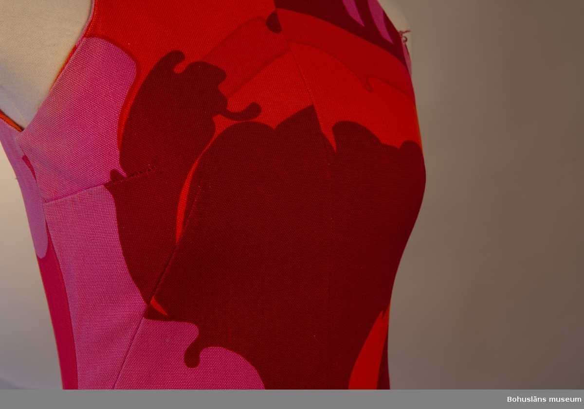 Stormönstrad långklänning i styvt bomullstyg med röd botten. Rak passorm med något utsvängande kjolparti. Sydd av fyra avlånga våder.
